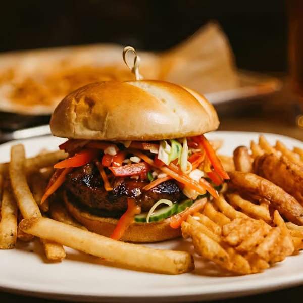 A gourmet burger with colorful slaw and fries on a white plate.