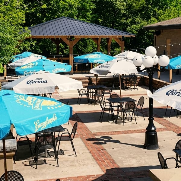 Outdoor patio with numerous tables, chairs, and umbrellas, some branded "Corona" and "Yuengling".