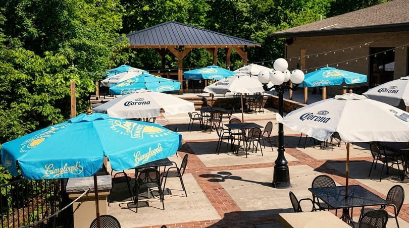 Outdoor patio with numerous tables, chairs, and umbrellas, some branded "Corona" and "Yuengling".