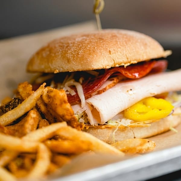 A deli sandwich with turkey, salami, and yellow peppers, served with a side of fries.