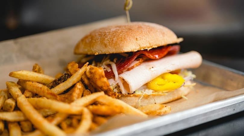 A deli sandwich with turkey, salami, and yellow peppers, served with a side of fries.