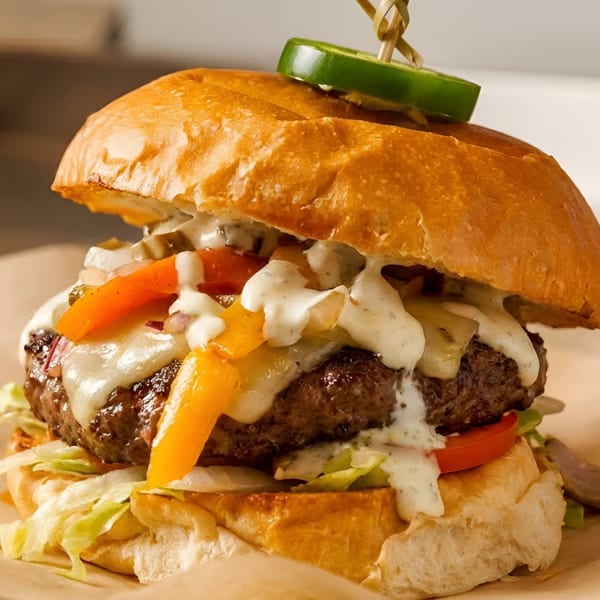 A juicy burger with melted cheese, colorful bell peppers, and a jalapeño slice on top.
