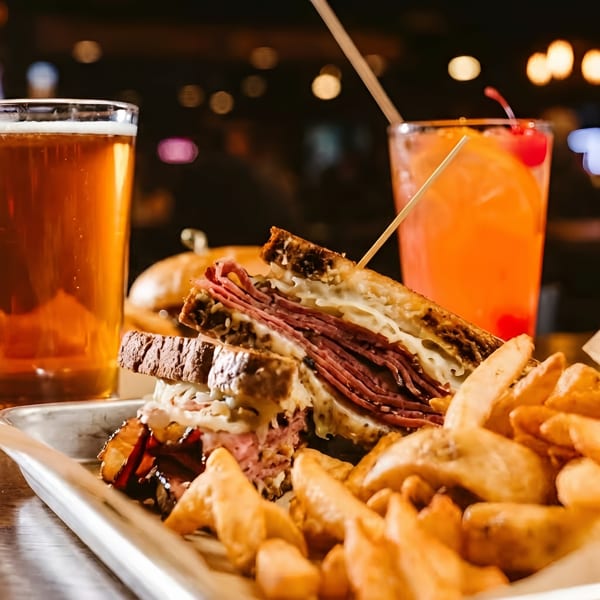 Reuben sandwich with fries, a beer, and a cocktail on a metal tray at a restaurant.