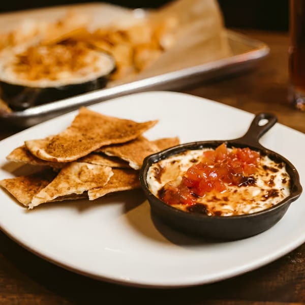 Baked dip with diced tomatoes in a cast iron skillet, served with tortilla chips.