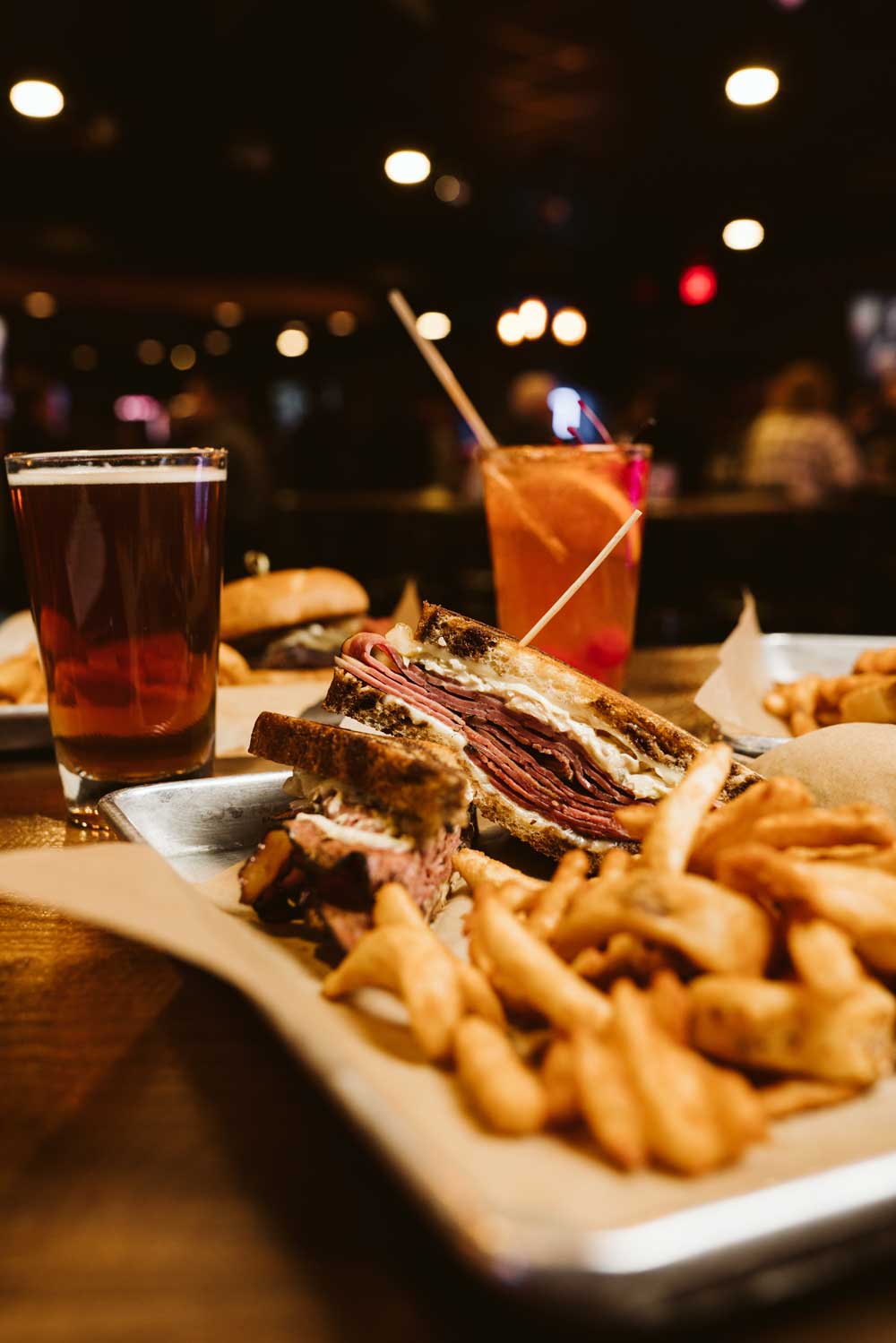 A tray at Plank Road Pub & Grill with a sandwich, curly fries, beer, and a cocktail.